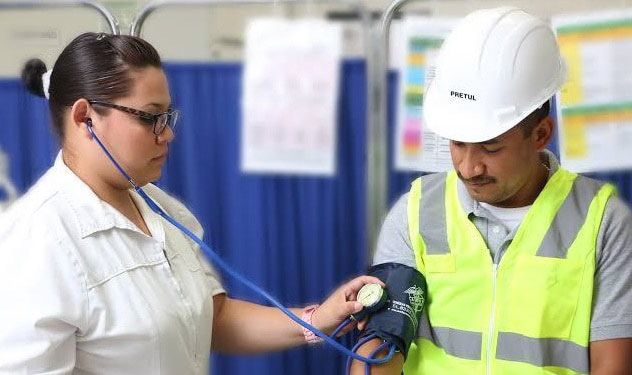Profesional de salud tomando la presión arterial a un trabajador con casco